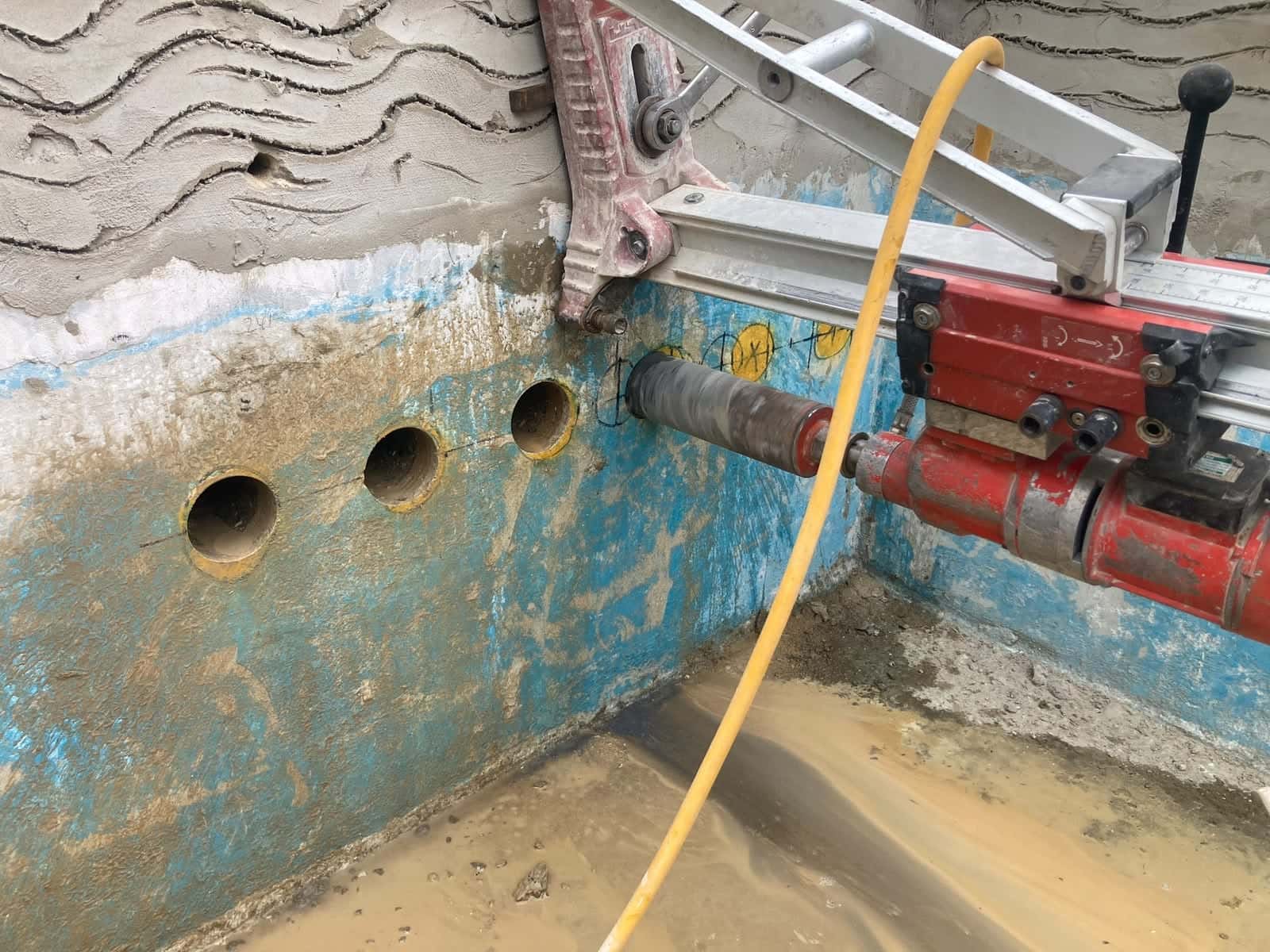 Core drill rig mounted on a concrete wall, set up to drill the next hole in a row of low-level cores