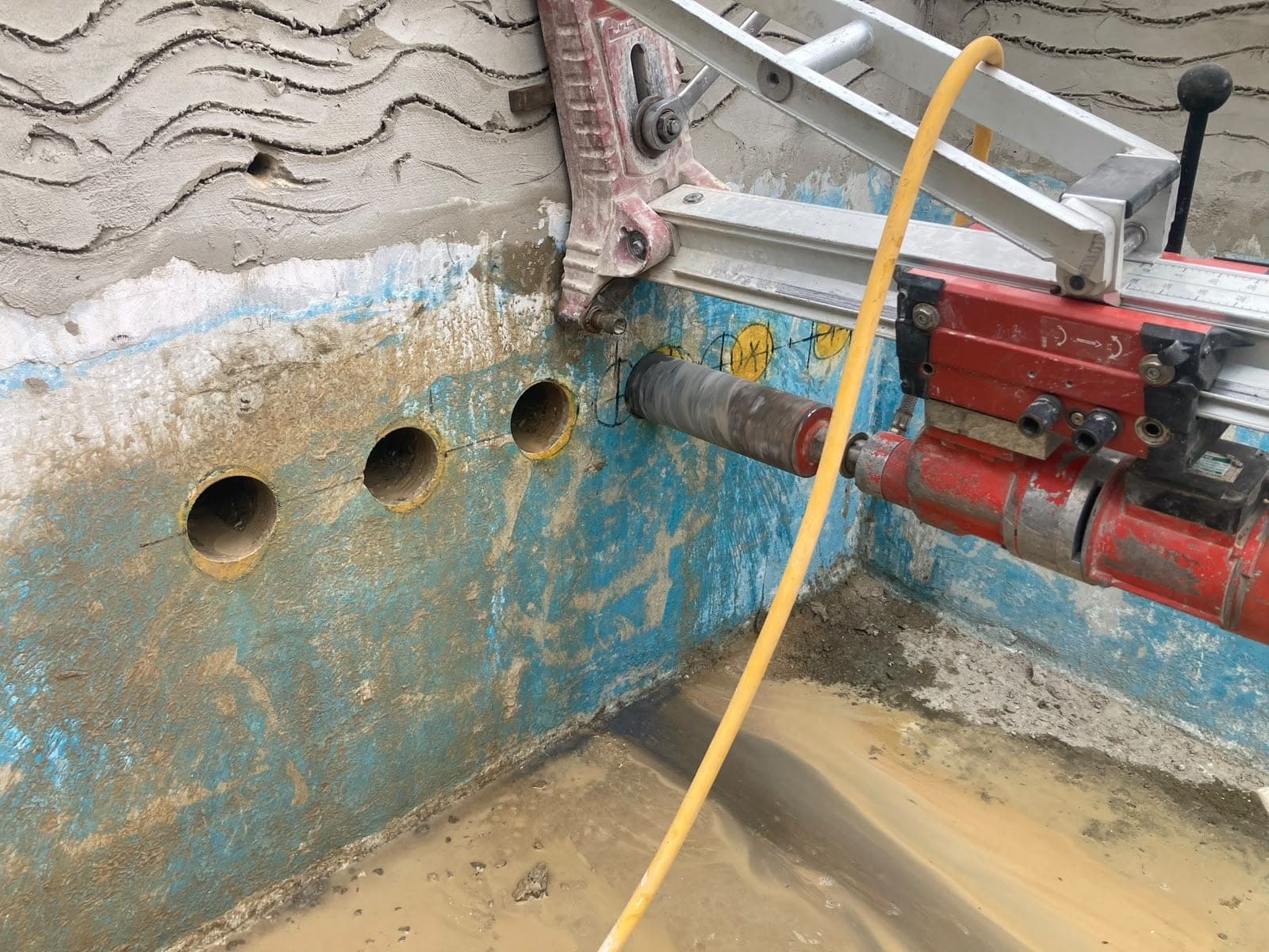 Core drill rig mounted on a concrete wall, set up to drill the next hole in a row of low-level cores