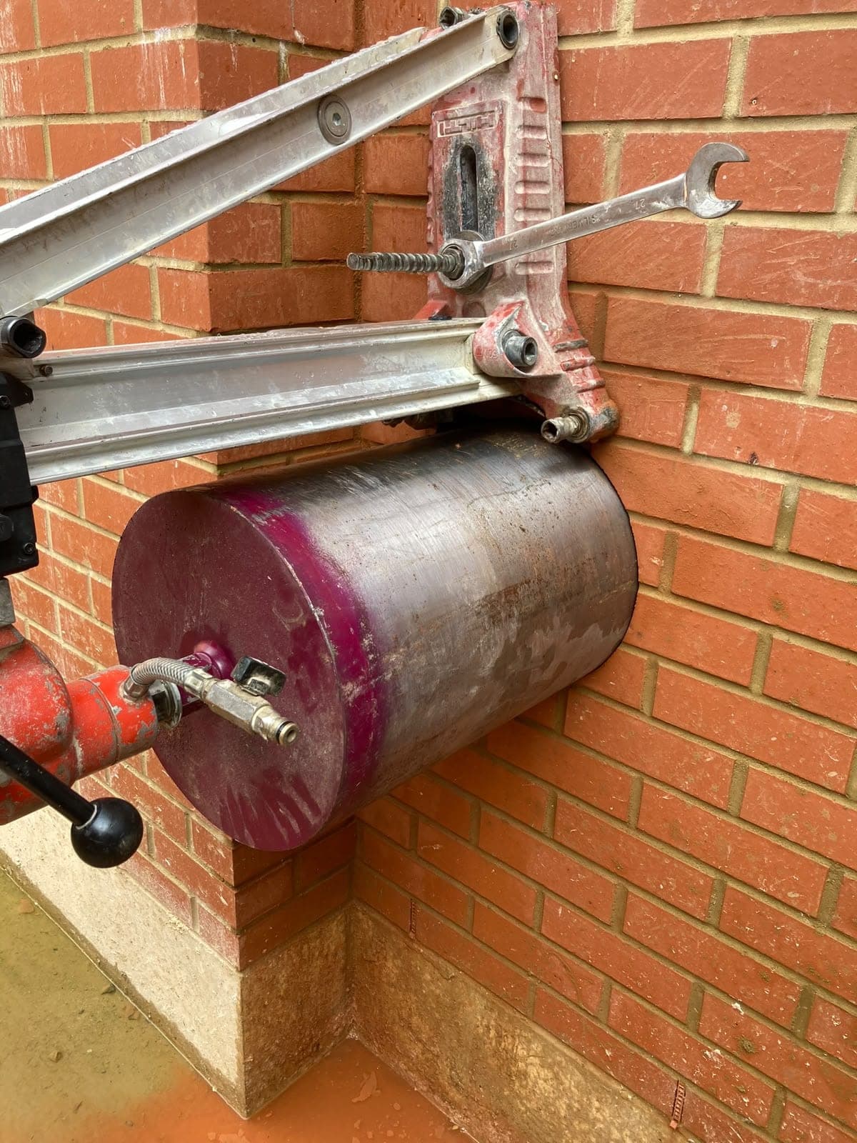 Large-diameter diamond core bit on a wall-mounted rig drilling through red brickwork
