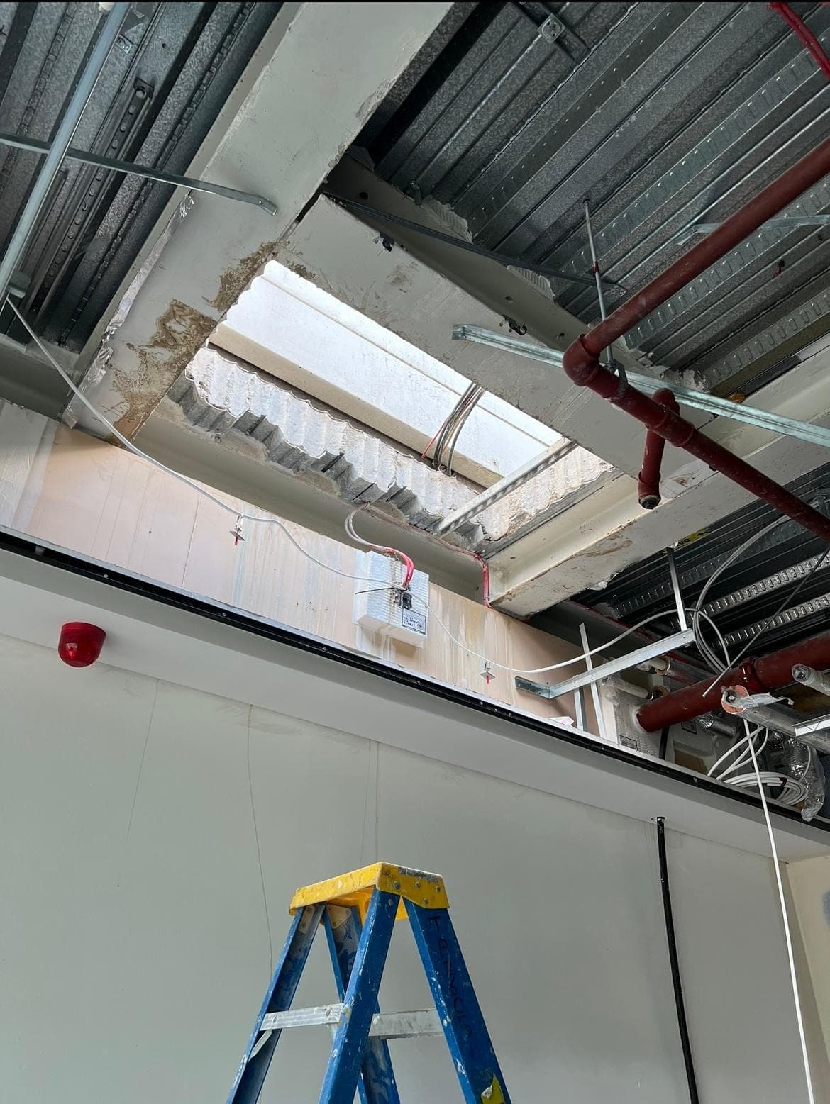 View from inside the building up through a new roof-slab opening, with metal deck ceiling and red sprinkler pipes