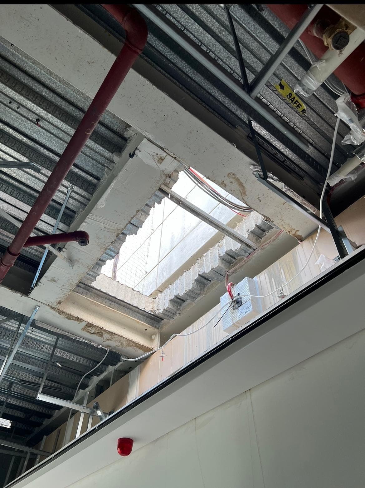 Underside view of an opening through a roof slab, with metal deck ceiling and service pipes