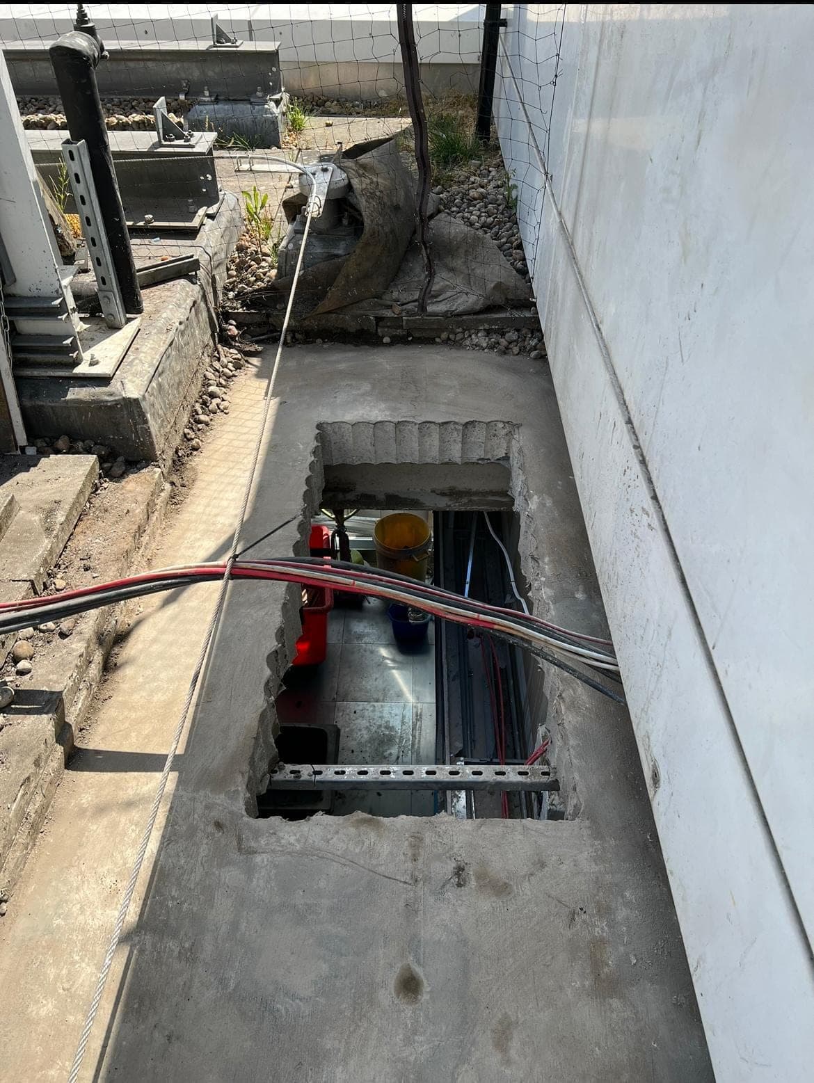Long rectangular stitch-drilled opening in a concrete roof walkway slab next to building cladding