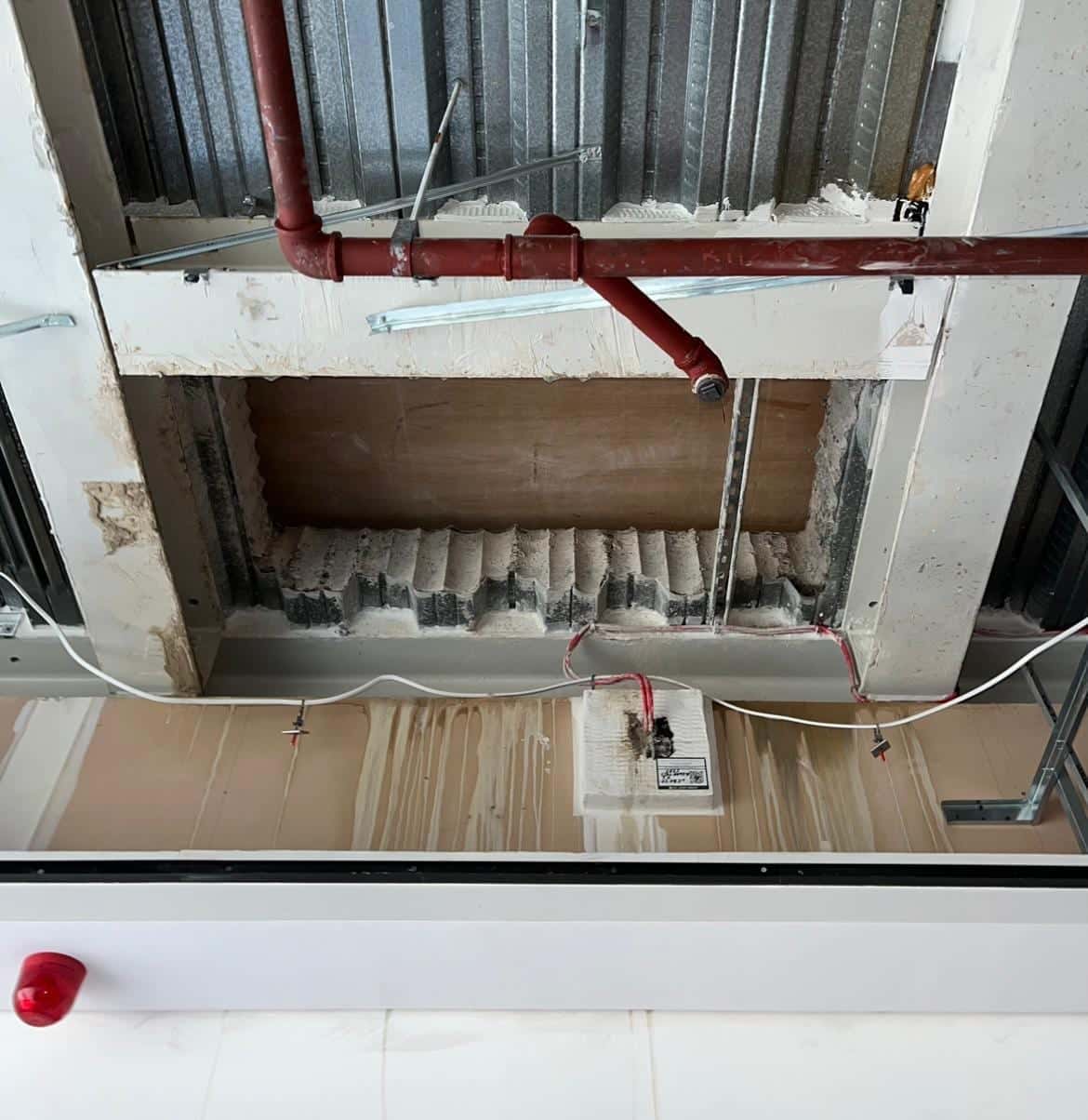 Underside of a long stitch-drilled opening seen from the floor below, with service pipes running past