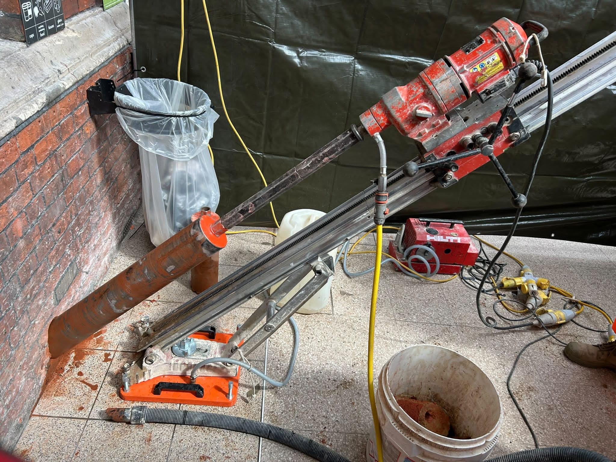 Angled core drill against a brick wall, with the vacuum hose connected to the rig’s orange base